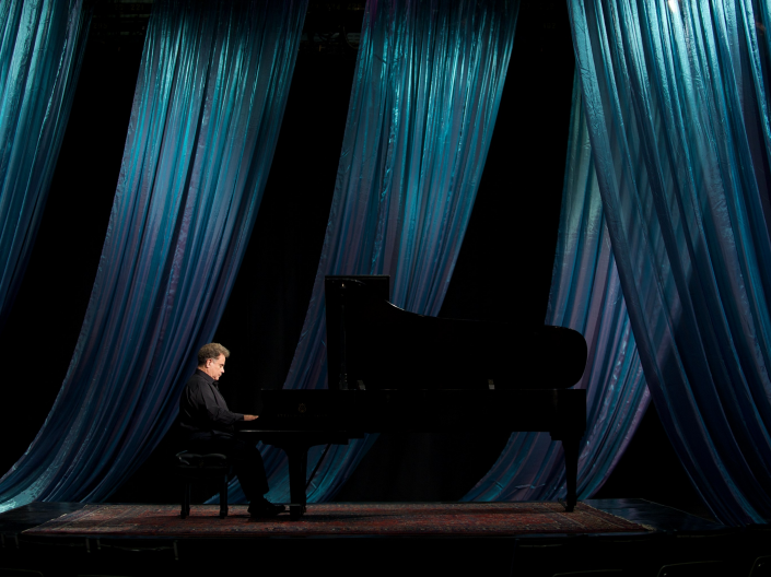 Jeffrey Siegel playing piano with a curtain behind him