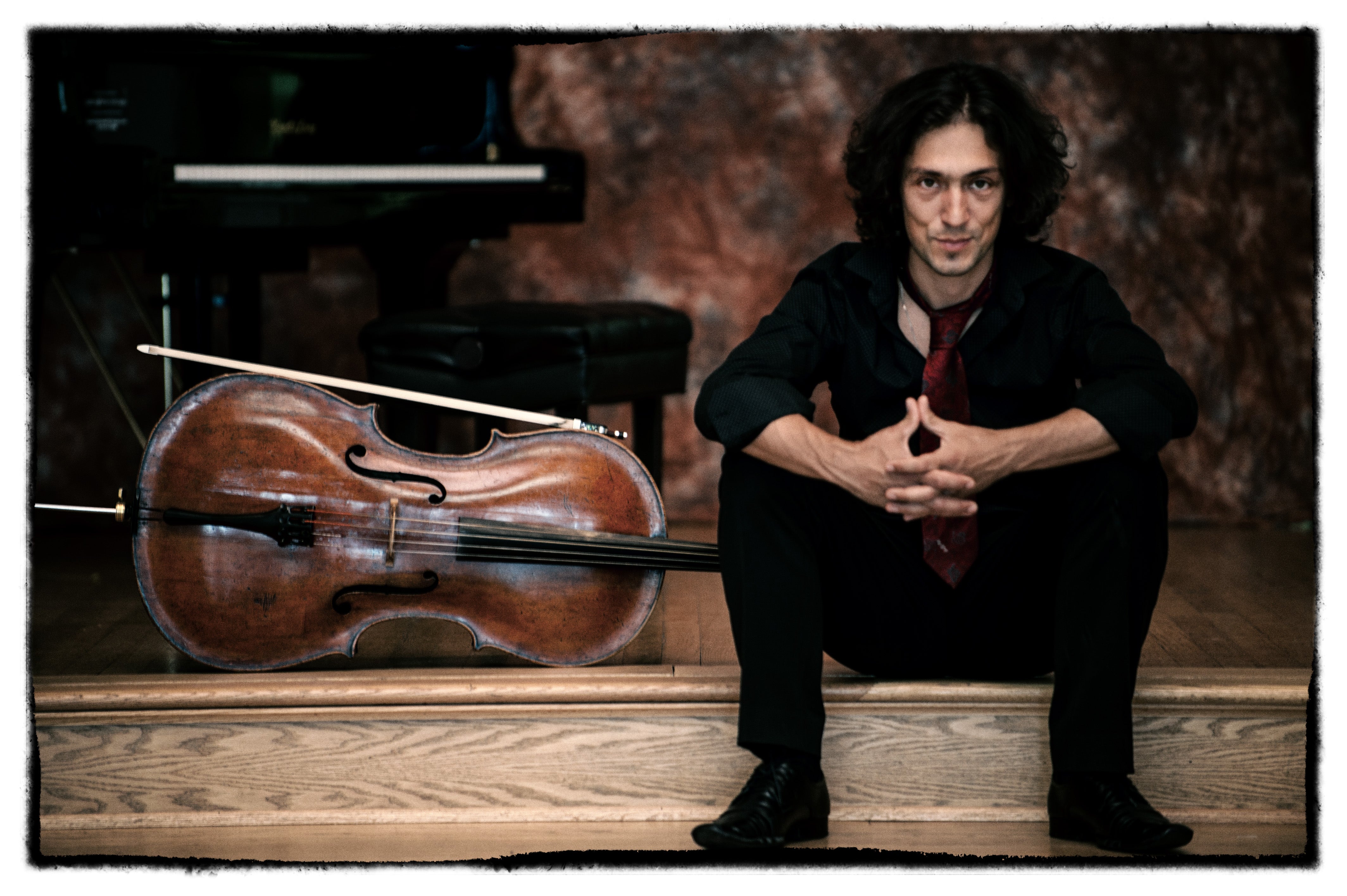 Ian Maksin sits on stage beside cello