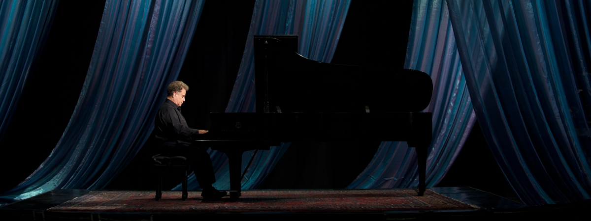 Jeffrey Siegel playing piano with a curtain behind him