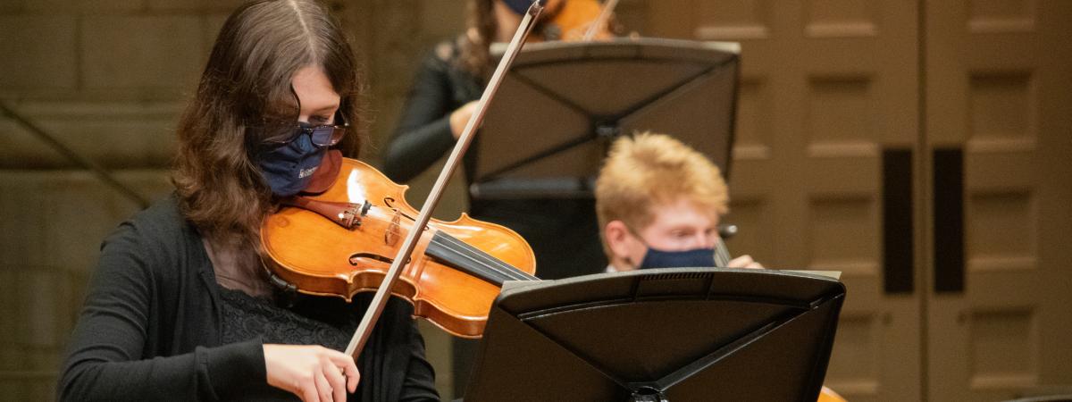 a violin player playing her violin with a cello player in the background