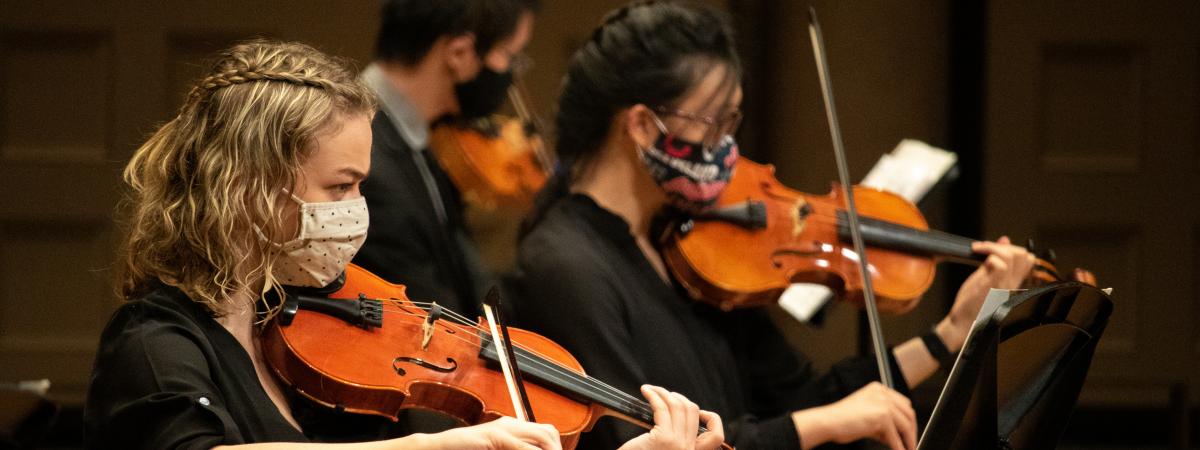 a violin player in the foreground with two more people playing violin behind that person