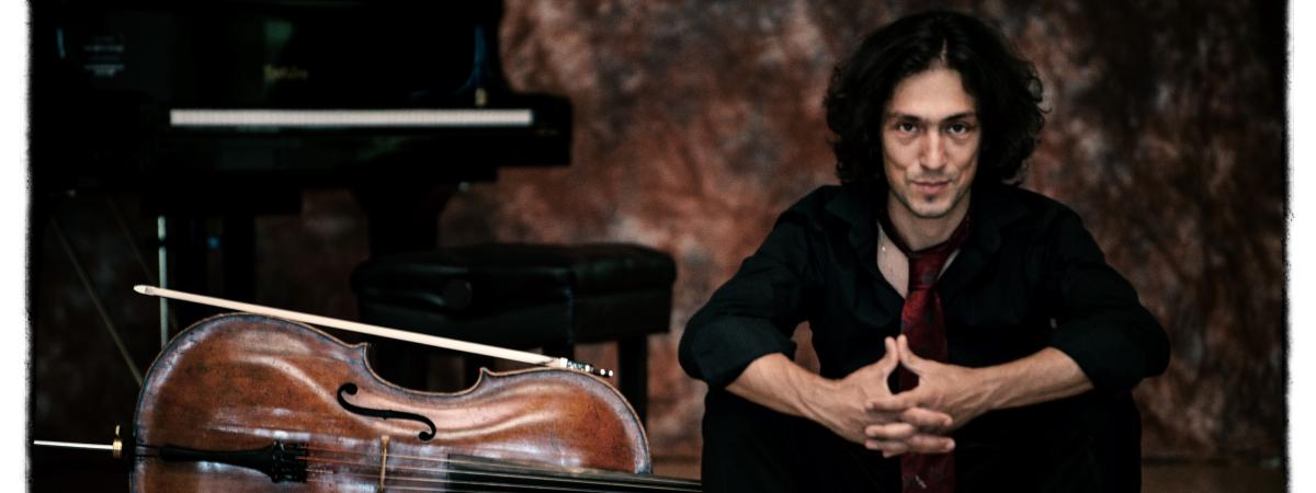 Ian Maksin sits on stage beside cello