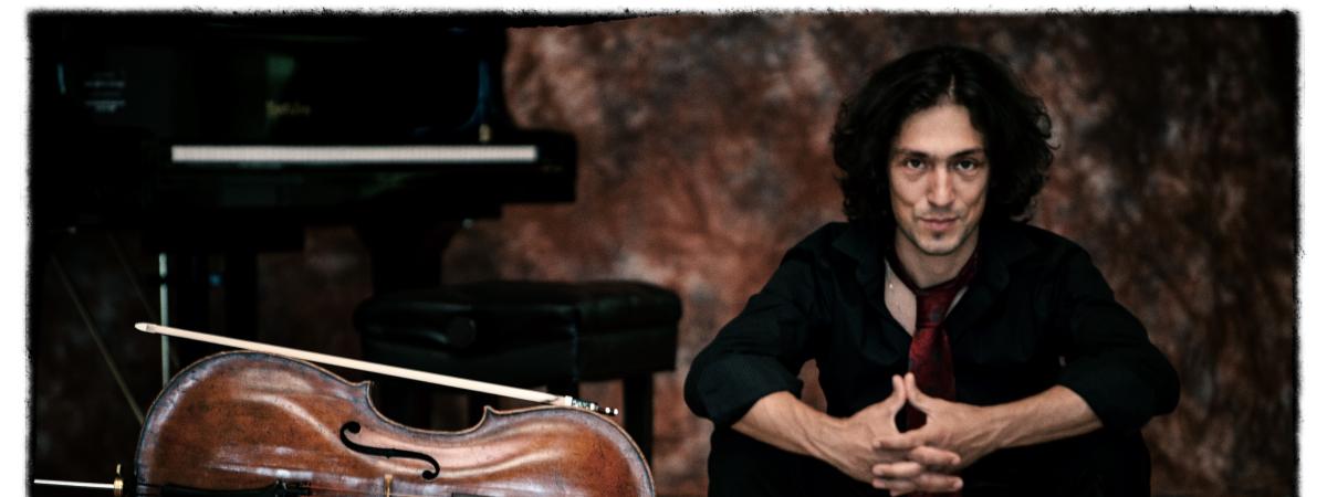 Ian Maksin sits on stage beside cello