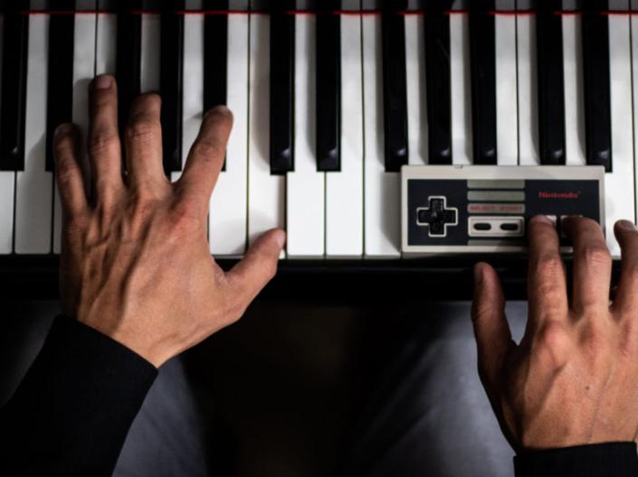 hands on piano keyboard with one hand on a Nintendo controller