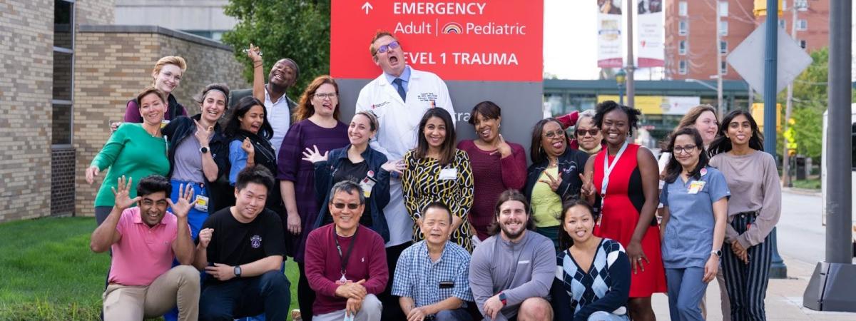 Twenty two members of the Remy Lab standing in front of the University Hospitals Cleveland Medical Center Emergency directional sign.