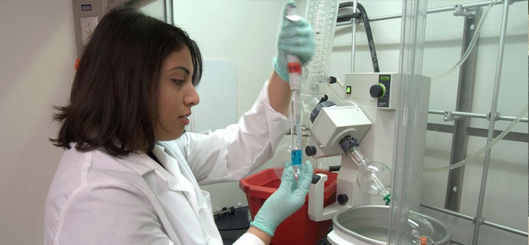 Student in lab coat performing lab tasks.