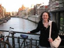 A girl standing on a bridge over looking the river.