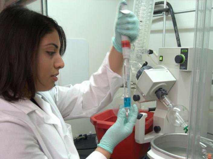 Student in lab coat performing lab tasks.