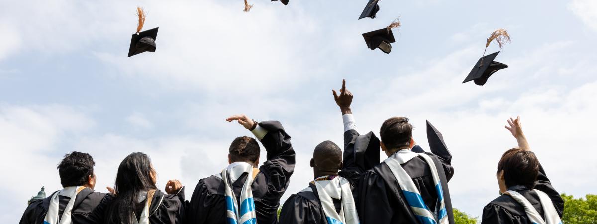 Students in graduation gowns tossing caps into the air