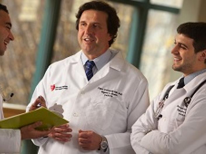 Image of Fabio Cominelli and 2 medical colleages, all in white lab coats, the 2 colleagues with stethescopes around their necks, one with a yellow clipboard, speaking in an open medical area