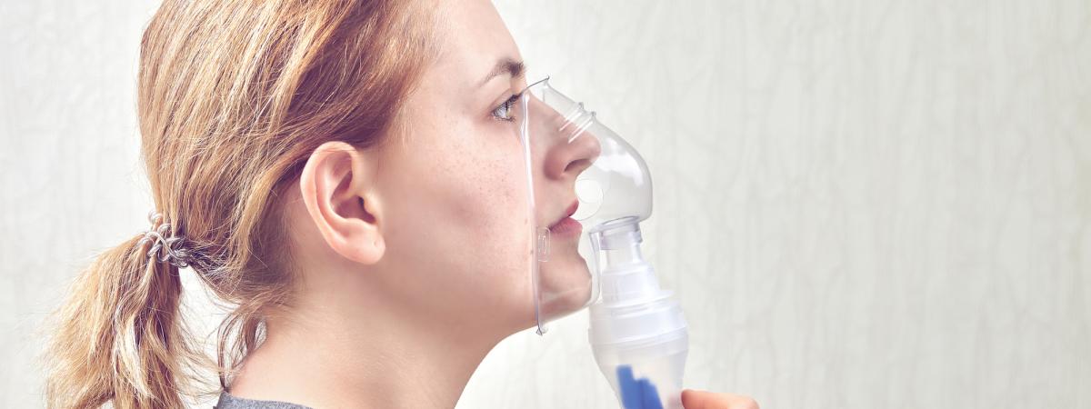 Close up of a feminine presenting person using an inhaler nebulizer for treatment respiratory disease