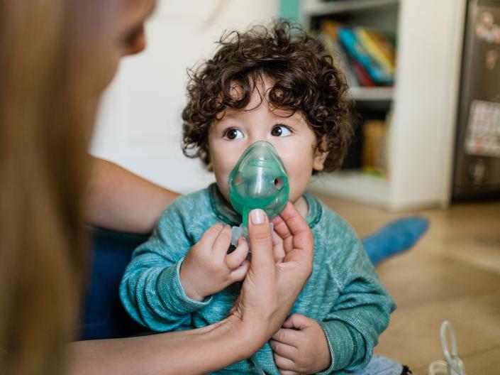 A young close up of a young child using a nebulizer with the help of an adult