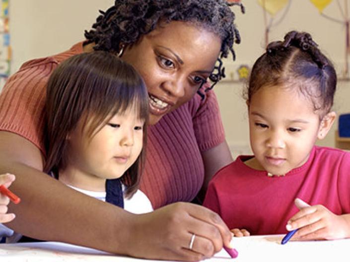 Photo of an adult coloring with two diverse children