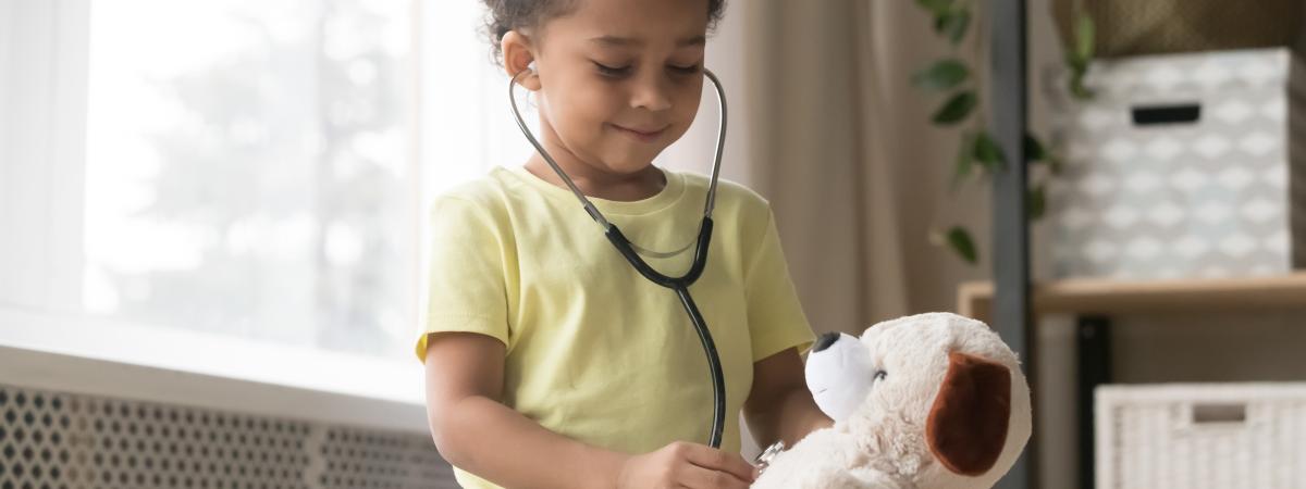 Photo of a smiling child using a stethoscope on a teddy bear