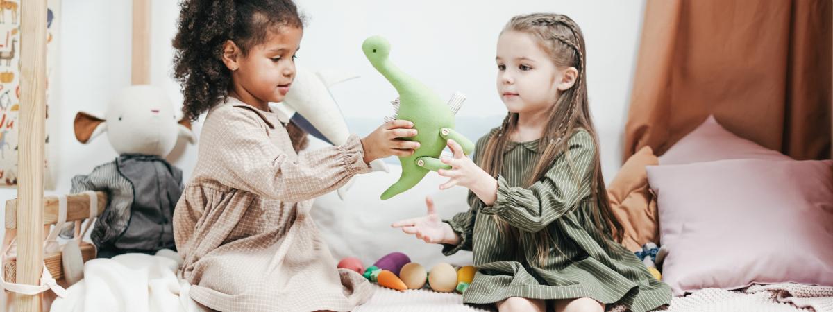 Two young kids sharing a toy dinosaur