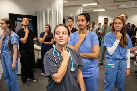 Medical students in scrubs gathered in a room, all pointing to their throats