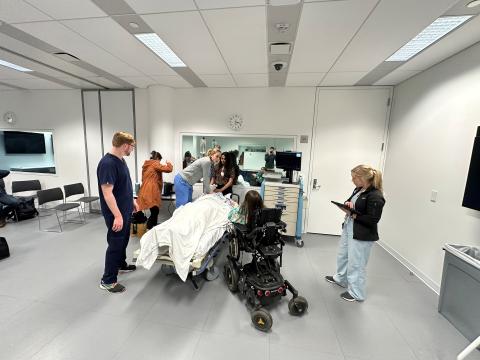 Students at a transition to residency session around a task trainer in an exam room.