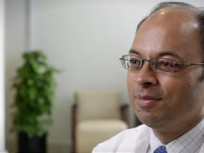 Image headshot of Dr. Mukesh K. Jain, door, medium sized potted plant, and biege chair with brown arms in the background