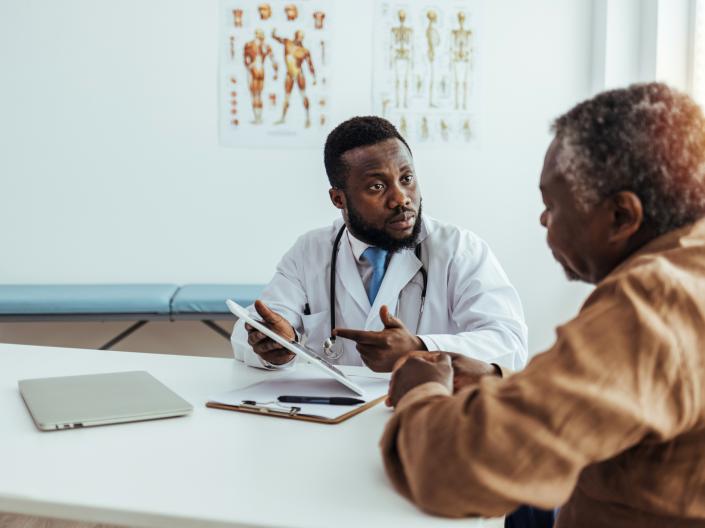 A black, masculine doctor reviews medical history with a senior patient of color