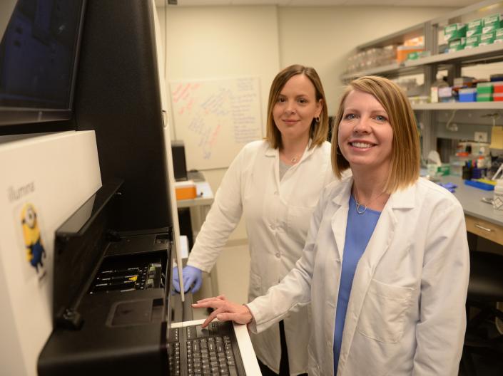 Two core employees wearing lab coats standing in front of an instrument.