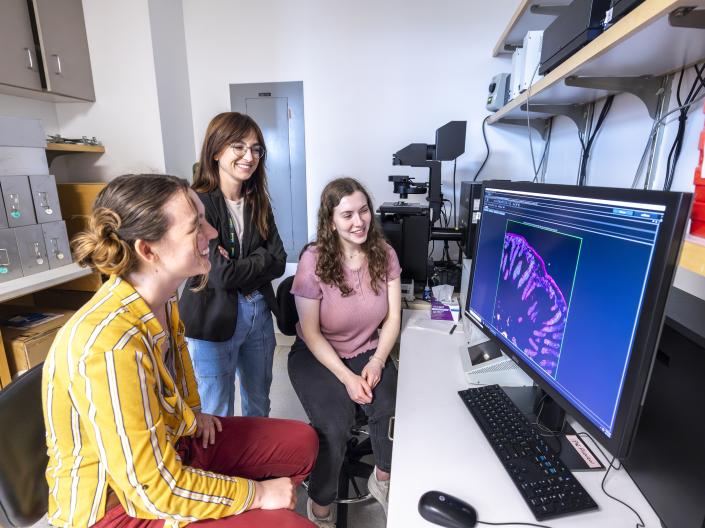 Three smiling women look at a computer monitor