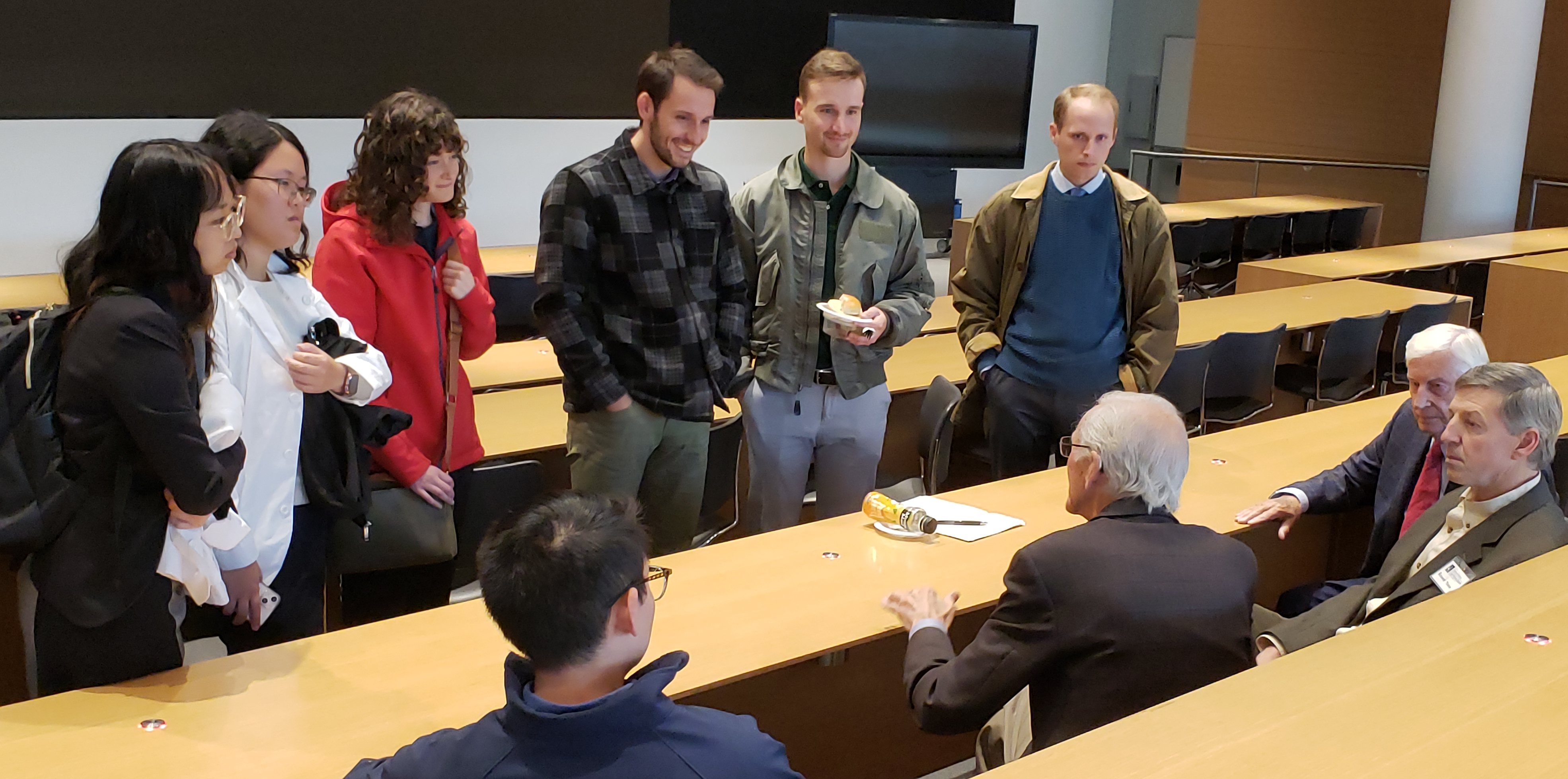 6 young people standing and talking with older board members, who are seated