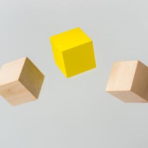 Picture of 5 wooden blocks in the air. The block in the middle is yellow, the others are natural wood color.
