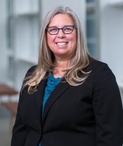 smiling woman with glasses, long hair, and dark suit