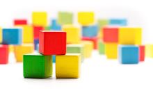 Picture of colorful wooden blocks. In the foreground, a red block is stacked on top of 2 blocks that are yellow and green.