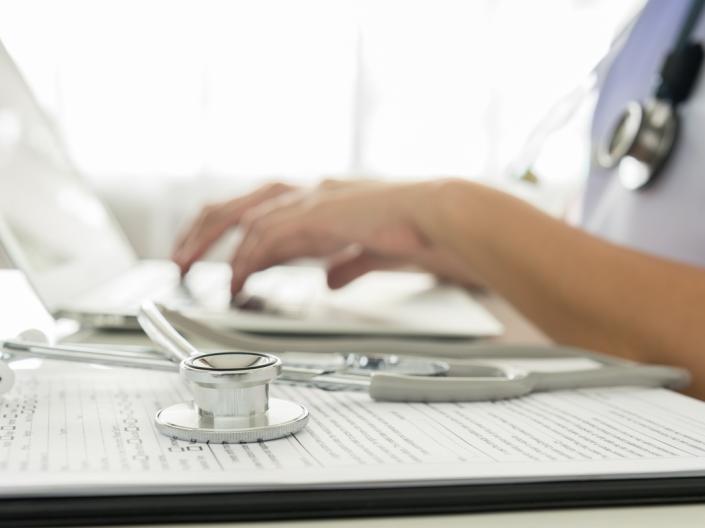 Close up of hands typing on a computer next to a stethoscope