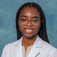 Woman with long dark hair and glasses in a white coat