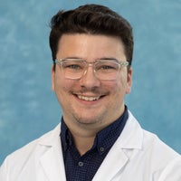 Man with short dark hair and glasses in white coat