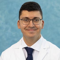 Man with short dark hair and glasses in white coat