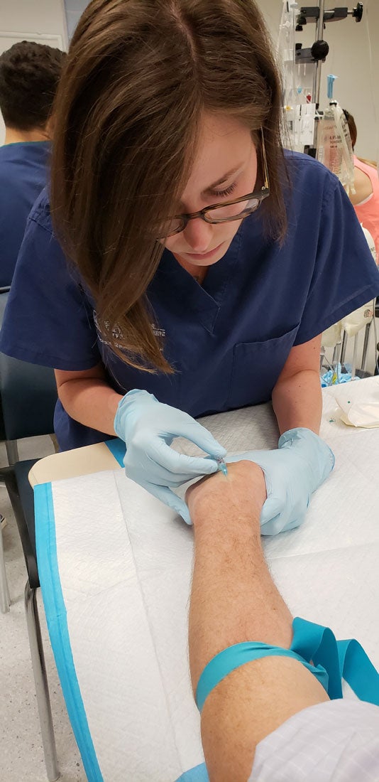 Female certified anesthesiologist student placing IV in hand
