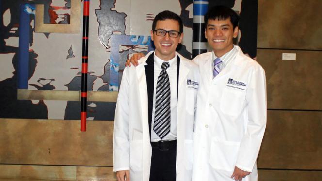 Two male Master of Science in Anesthesia students posing in their white coats in front of artwork