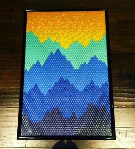 Artwork of mountain range in yellow, green, and blues made partially from recycled caps
