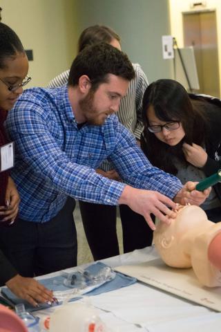 Male student showing three prospective students an anesthesia task trainer