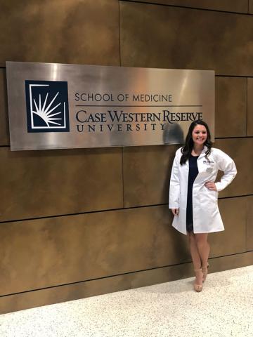 Female certified anesthesiologist assistant student in white coat standing at Case Western Reserve University sign