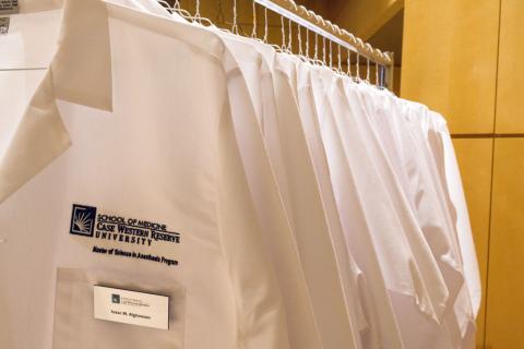Row of white coats on hangers with School of Medicine Case Western Reserve University embroidered on front with name tag