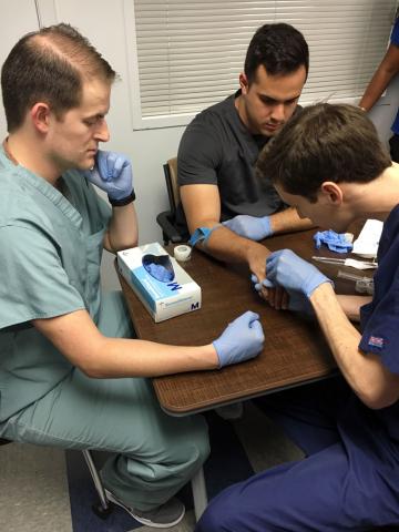 Male Master of Science in Anesthesia student practicing IV on hand while male certified anesthesiologist assistant observes