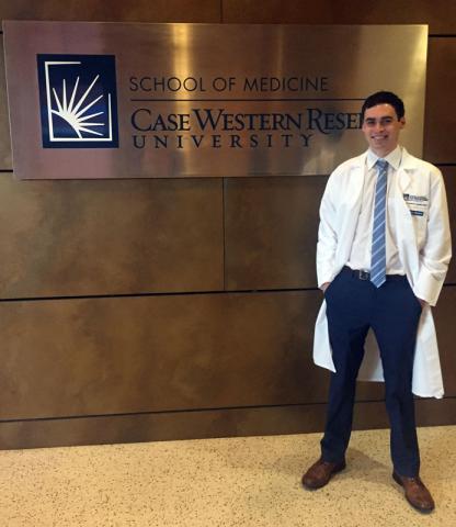 Male Master of Science in Anesthesia student in white coat with sign reading School of Medicine Case Western Reserve University