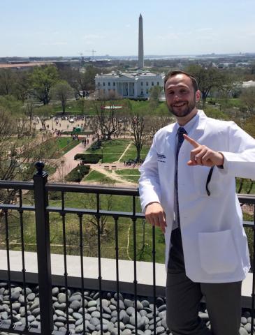 Male Master of Science in Anesthesia student in white coat in front of Washington monument in Washington, D.C.