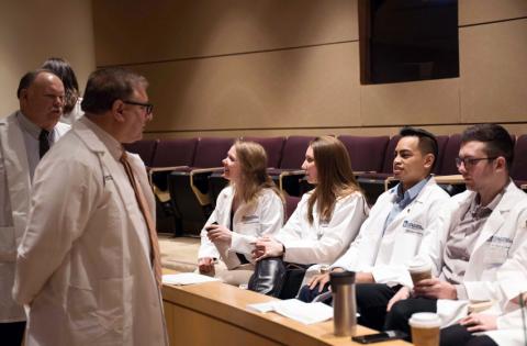 Four CWRU MSA students in white coats speaking with two faculty members