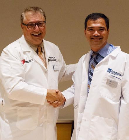 Two male certified anesthesiologist assistants in white coats shake hands