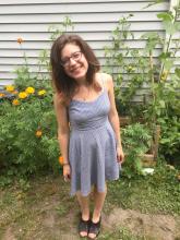 A smiling woman with glasses and brown hair stands in front of a garden