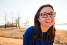 Photo of a smiling woman with glasses standing in front of a body of water in winter