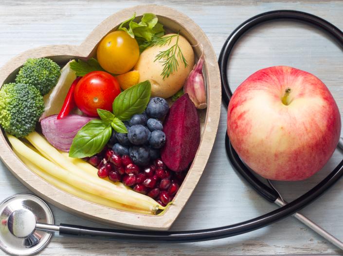 a heart-shaped bowl of fruit arranged with a stethoscope and a single apple