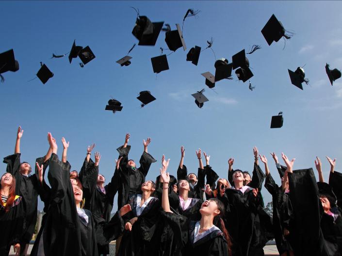 A group of students in graduation gowns toss their hats in the air.