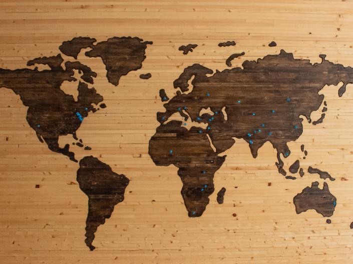 A wooden world map with blue pushpins stuck in various locations.