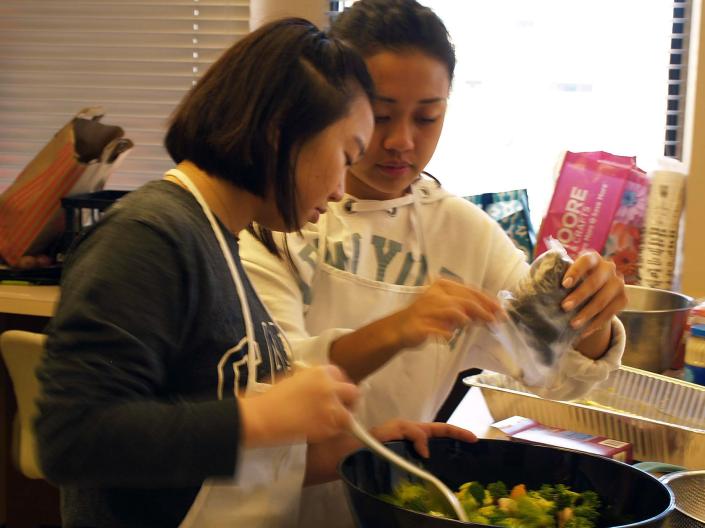 Two students work together to make a large bowl of salad.
